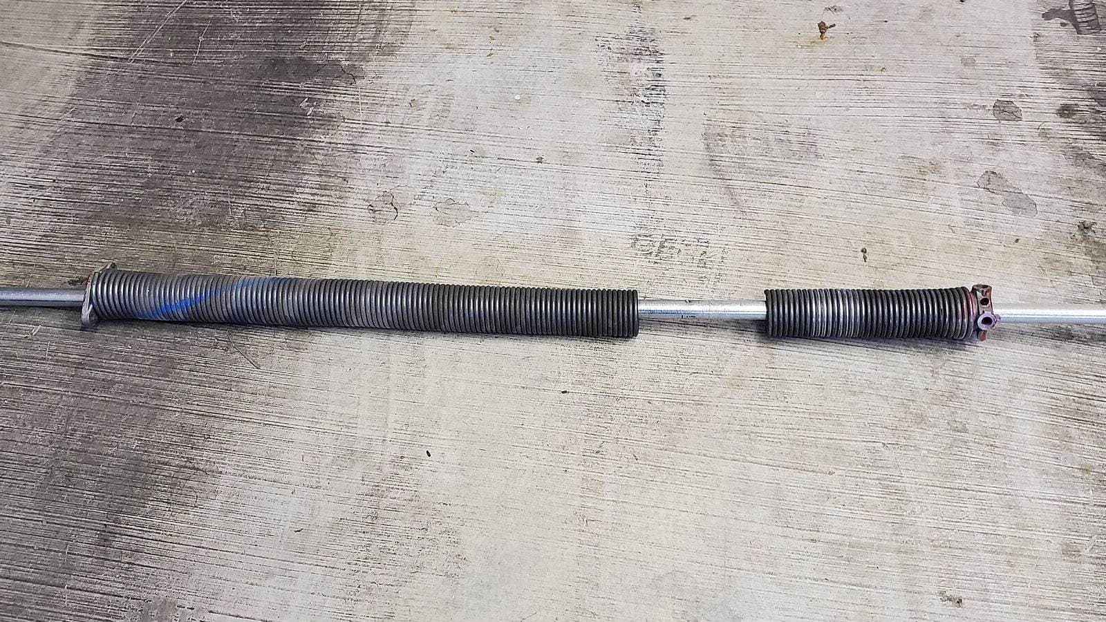 Snapped garage door torsion spring on its shaft, with a clear gap where the coil broke in two